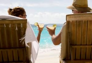 2 Canadian Dividend Stocks I’d Invest In and Keep for the Long Term people sit in two wooden beach chairs facing the Caribbean ocean holding drinks and making a toast