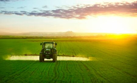 Tractor spraying a field of wheat with fertilizer